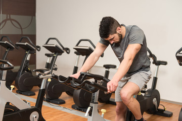 Naklejka na ściany i meble Muscular Man Doing Cycling In Modern Fitness Center