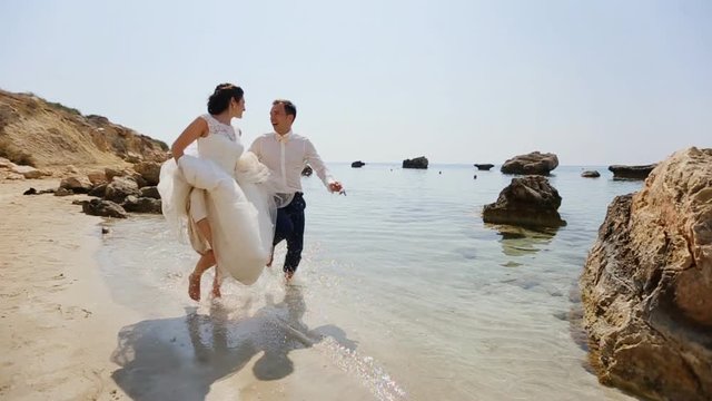 adult male groom and female bride running barefoot on beach