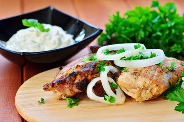 Skewers with onions and parsley on a wooden table. White sauce and a bunch of parsley in the background
