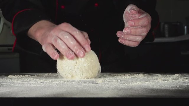 SLOW: A baker is kneading a dough on a cutting board in a kitchen