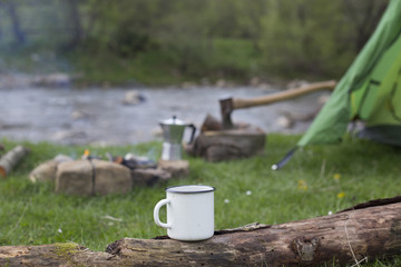 Mug stands on a log near the fire at a campsite.