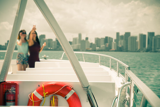 Vintage style image of inside of boat with indistinguishable females posing for a selfie and Miami city skyline in the background