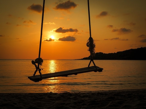Silhouette of rope swing hang over beach at sunset.