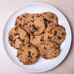 top view of chocolate chip cookies on white plate on wooden tabl
