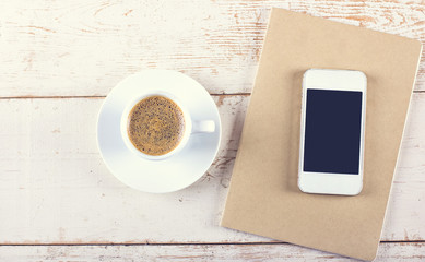 Smart phone with notebook and cup of strong coffee on wooden background. Cellphone with writing set with espresso