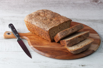 Homemade dark rye sourdough bread on wooden chopping board with kitchen knife