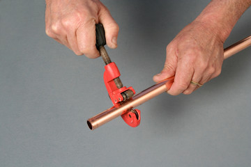 Plumber cutting a copper pipe with a pipe cutter.