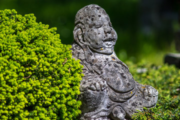 Buddah sitting in aisan garden next to green