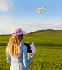 Young woman holding radio controller with tablet and sun shade flying drone uav over a field. Aerial video and photography maker. Hovering aircraft in the background.