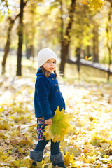 little girl keeps leafs in hand in park in the autumn