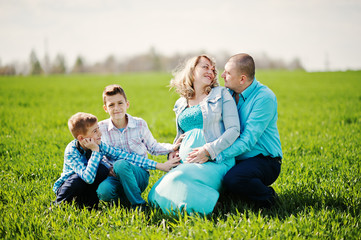 Naklejka na ściany i meble Happy pregnant family with two sons, dressed in a turquoise clot