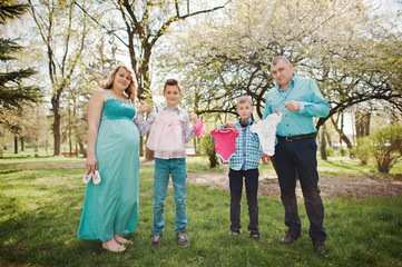 Happy pregnant couple with two sons holding girls' baby clothes