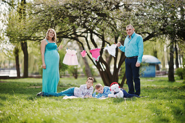 Happy pregnant couple with two sons holding girls' baby clothes