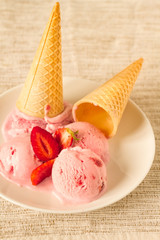 Two cones with strawberry ice cream turned upside down and fruits on a plate 
