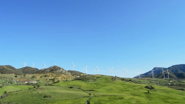 Landscape of wind turbines energy in a green field together mountains and a road at sunny day