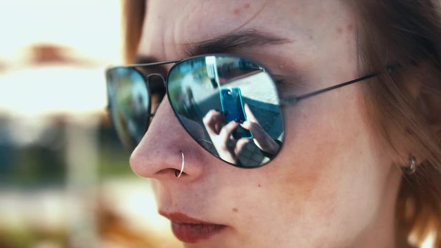 Young attractive Caucasian female texting on the phone, as seen in sunglasses reflection. 60 FPS slow motion shot. Blackmagic URSA Mini graded footage