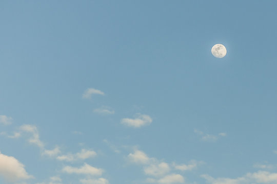 The moon appears in a clear sky at sunset in the beach