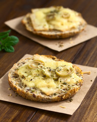 Vollkornbrot überbacken mit Schinken, grünen Oliven, geriebenem Käse und Oregano, fotografiert mit natürlichem Licht (Selektiver Fokus, Fokus auf die Olivenscheiben auf dem ersten Brot)