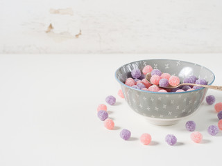 Round purple and pink bonbon candies in a bowl on white rustic background, copy space