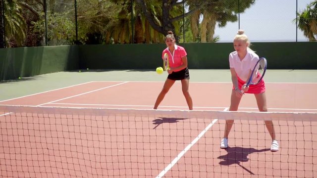 Two attractive shapely young women playing a game of tennis doubles standing ready to receive service
