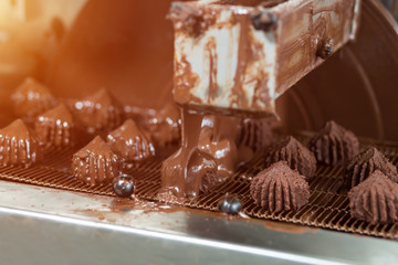 Machine pouring liquid on candies. Conveyor belt with brown sweets. Production of high-quality dessert. Under a flow of chocolate.