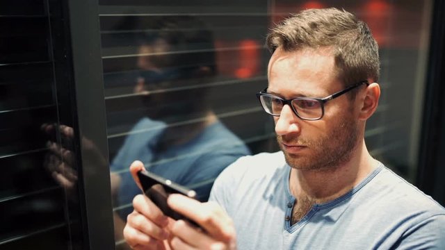 Man standing next to the window and texting on smartphone
