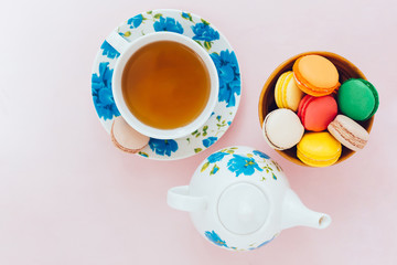 Colorful macaroons with cup of tea on pastel background