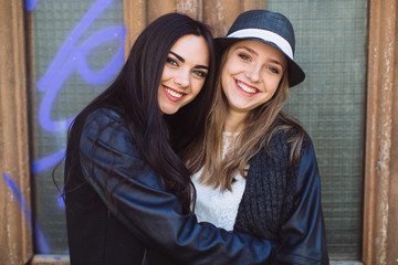 Two stylish and happy street girls posing at the wall. Sisters.