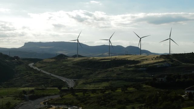 Wind turbines energy moving at the mountain together a road at cloudy day