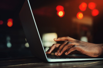 Black man's hands typing on laptop keyboard. Person working with laptop. Beautiful lights as background. Toned style instagram filters 