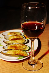 Mussels baked with cheese on the white dish and glass of grape juice