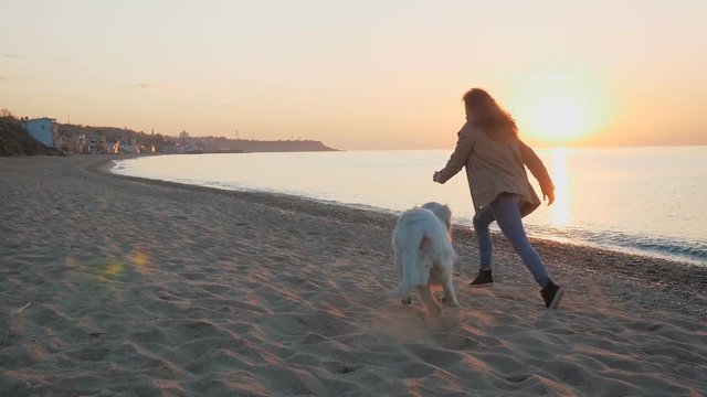 Young female running and playing with retriever dog on the beach during sunset or sunrise, slow motion