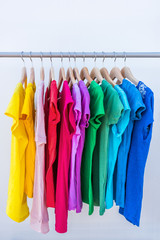 Fashion clothes on clothing rack - bright colorful stand of rainbow selection of t-shirts. Choice of trendy female wear on hangers in store closet or spring cleaning concept. Summer home wardrobe.