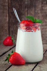 Small jar on wooden table with yogurt with fresh strawberry