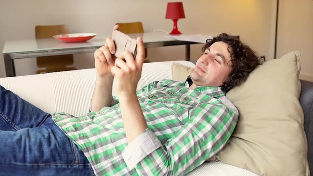 Happy man texting on smartphone and lying on the sofa
