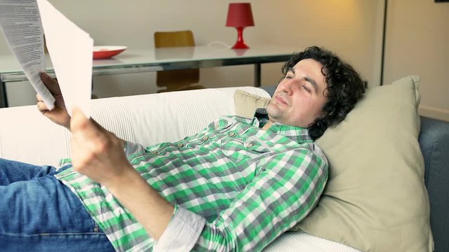 Upset man lying on the sofa and reading documents
