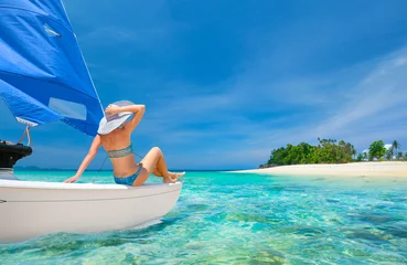 Wall murals Sailing Woman traveler sit at the stern of sailboat looking to the beach
