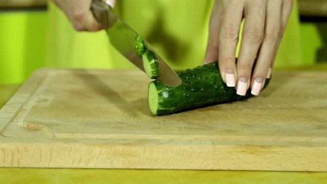 Woman slicing cucumber. Female hands cut green cucumber rings. Big knife. In the kitchen. Wooden board. house-proud woman. Fresh cucumber. Fresh vegetables. sharp knife.