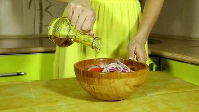 Woman pours salad oil. Female hands watering vegetables oil. Wooden salad bowl. Fresh vegetables. Olive oil. Oilcan. Tomatoes, cucumbers, onion. bamboo bowl. In the kitchen. house-proud woman.