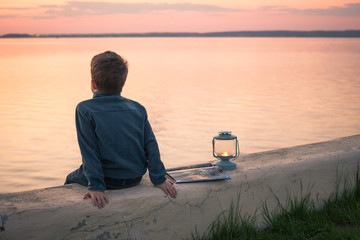 Fototapeta premium Child sitting enjoying orange sunset over water