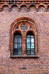 Window in an old red brick wall, with gothic elements as arch and rose windows