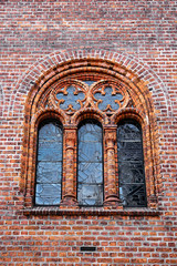 Ancient gothic inspired soft arched window with latticed glazing and small rose windows on top, situated in a red brick wall 