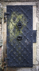 Historical house door. Big metallic old door. One timber leaf, closed black gateway with metal and nails. Exterior country situation. Rural entry architecture element. Village foundation background.