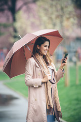 Young woman with umbrella at the park, using her mobile phone