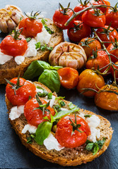 Toasts with feta cheese and small cherry tomatoes baked with garlic, salt and olive oil. Black stone background.