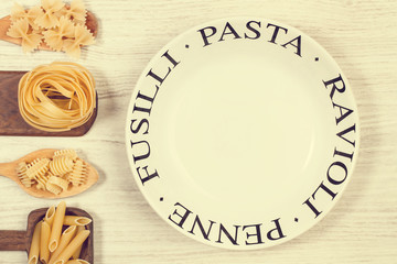 Pastas secas variedad sobre diferentes cuchara de madera rústica junto a un plato redondo con inscripcion Pasta. Vista superior