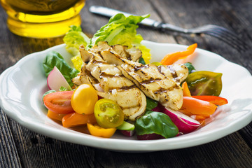 Delicious salad with grilled chicken breast on a wooden background