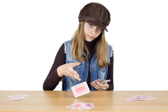 Young Girl Sitting At A Wooden Table And Dealing Playing Cards For The Next Round, Isolated On White