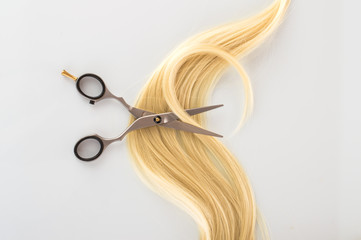 Hairdressing Scissors with a strand blond hair on a light background close-up
