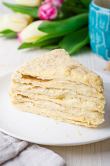 Slice of Napoleon cake with tulips on white vintage background. Selective focus